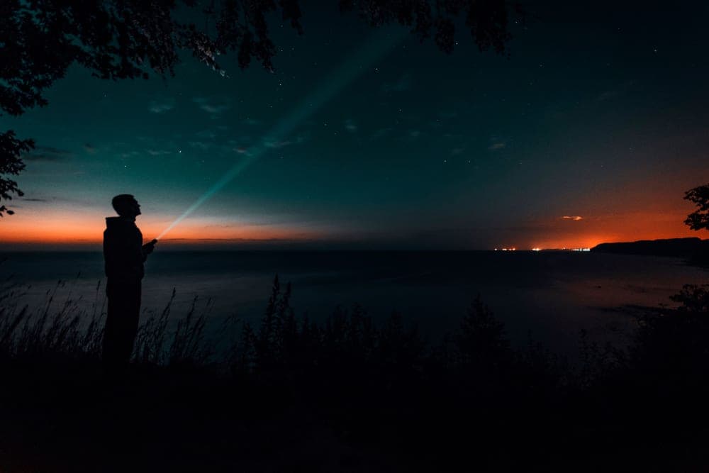A person with a flashlight under a starry twilight sky