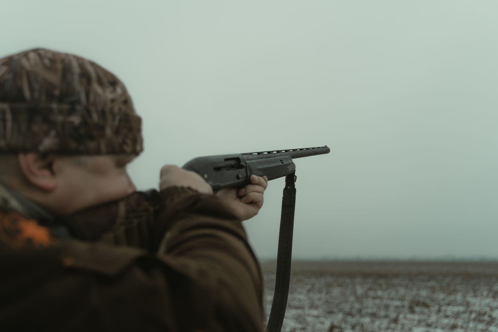 A hunter in camouflage aiming across an open field
