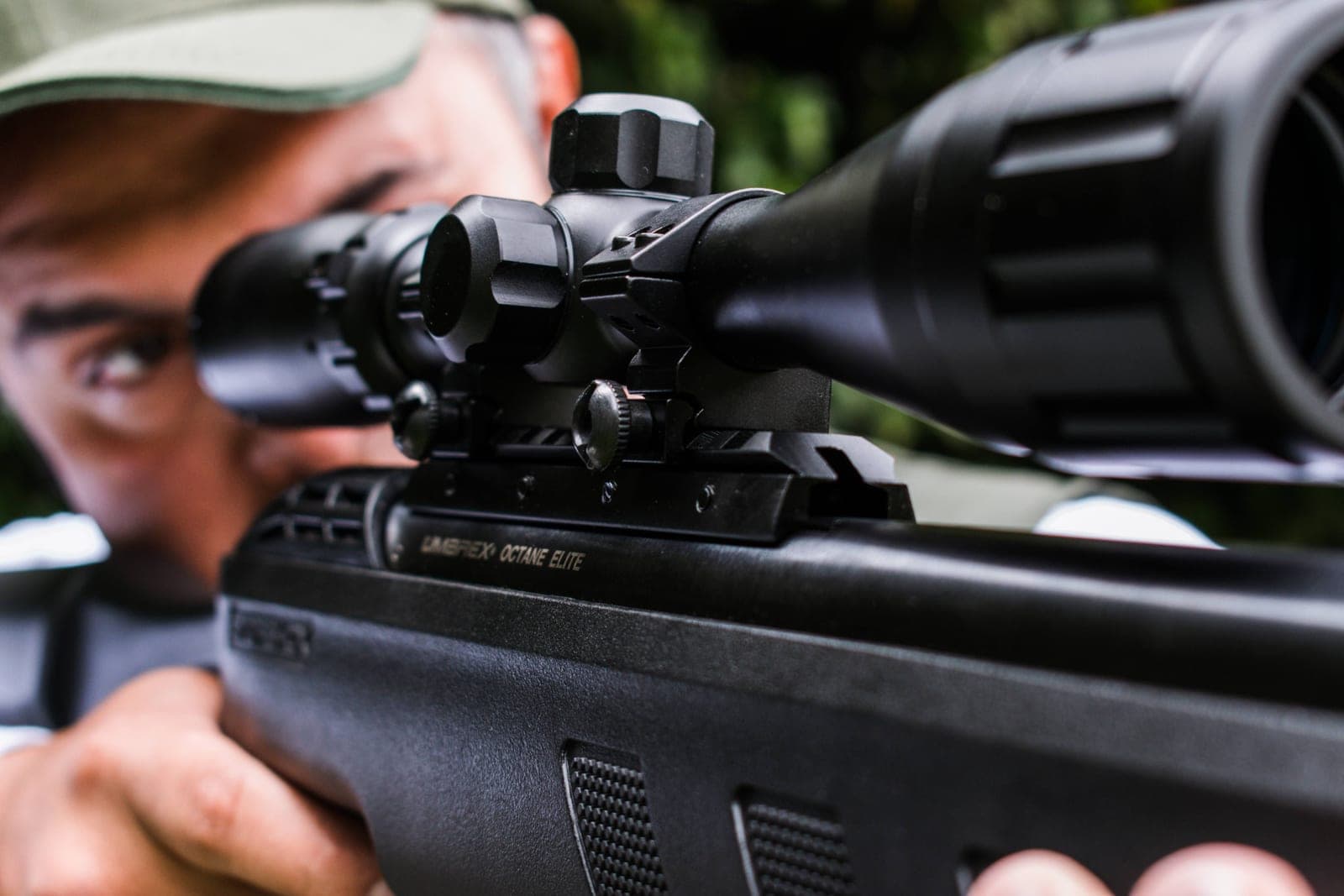 A man aiming a scoped rifle outdoors